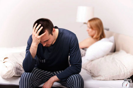 hombre sentado en cama con su mujer y preocupado por su perdida de sensibilidad en el pene
